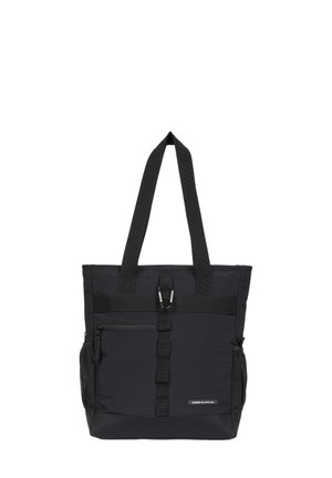 Bolsa de lona negra con dos asas para el hombro, bolsillo frontal con cremallera, bolsillos laterales de malla y un pequeño mosquetón de metal sujeto a la correa frontal.