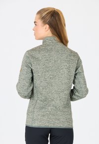 Grön heatherjacka med hög krage, texturerat stickat material och figursydd design. Har en logotypapplikation på vänster ärm.