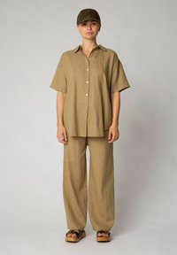 Khaaki Leinenhemd mit kurzen Ärmeln, knöpfbarem Vorderteil, kombiniert mit einer passenden weit geschnittenen Hose und einer enganliegenden Mütze, beides in der gleichen Farbe.