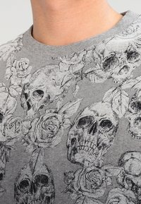 Grijs shirt met ronde hals met zwarte en witte gedetailleerde schedel- en rozenpatronen.
