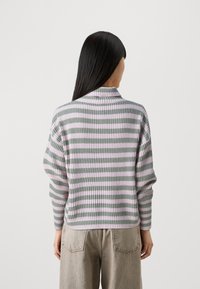 Striped, knit sweater in light pink and green. Features long sleeves, a high neck, and a relaxed fit. Fabric has a ribbed texture.