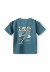 Teāls kokvilnas T-krekls ar īsām piedurknēm, aizmugurē ar baltu drukātu tekstu un grafiku, kas saistīta ar tenisa akadēmiju.
