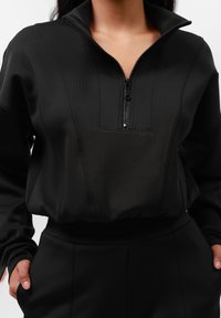 Zwarte rits-hoodie met een hoge kraag, gemaakt van gladde stof, met tonale stiksels en een gestructureerde pasvorm rond de taille.