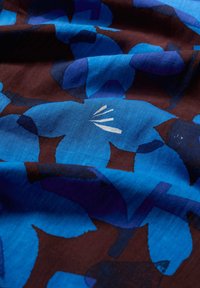 Blaues Blumenmuster auf einem dunkelbraunen Hintergrund mit großen, sich überlappenden Motiven. Der Stoff hat eine glatte Textur und einen lebendigen Farbkontrast.