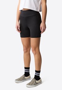 Svarta sportiga shorts med hög midja, tillverkade av töjbart material. Bärs med rutiga slip-on skor och svarta randiga strumpor.