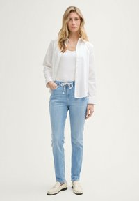 Bílá košile s knoflíky přes bílý tílko, doplněná světle modrými džíny s tkaničkami. Celý outfit doplňují béžové polobotky.