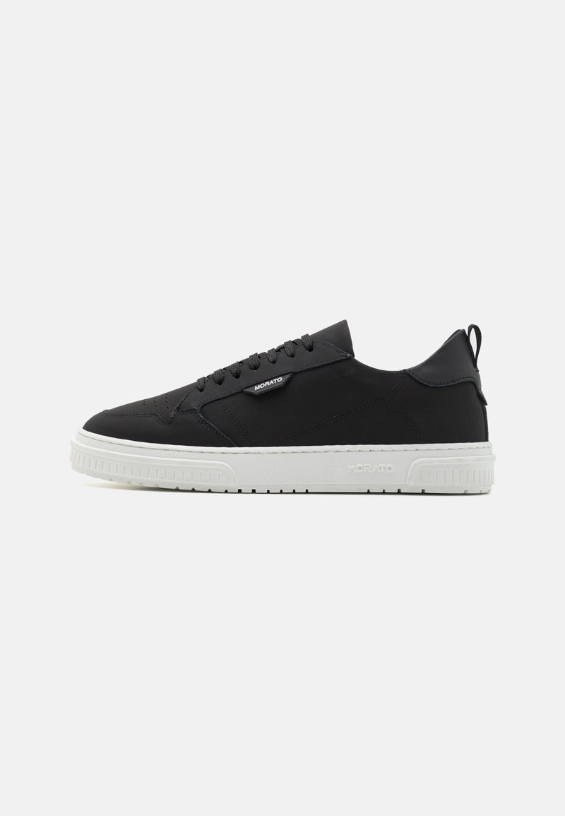 Baskets en cuir noir avec une semelle en caoutchouc blanche, présentant un bout rond, un laçage et une petite boucle à l'arrière pour un enfilage facile.