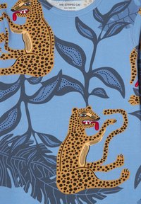 Tessuto blu con illustrazioni di leopardo in tonalità di marrone con macchie nere, circondato da foglie stilizzate verdi e uno sfondo semplice.