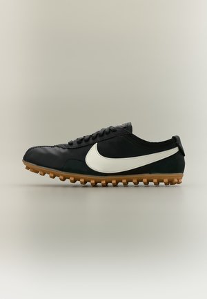 Czarny sneaker Nike z białym logo swoosh i gumową podeszwą widziany z boku na jasnoszarym tle.