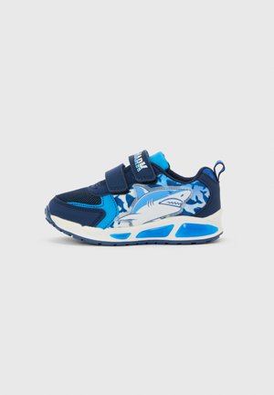 Børnesneaker i marineblå og lyseblå med hajgrafik, camouflage-mønster og to velcrolukninger på hvid sål.
