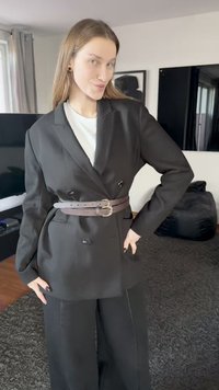 Veste blazer noire à double boutonnage avec une taille cintrée, associée à un pantalon noir à jambes larges. Comprend une ceinture en cuir marron avec double boucle.