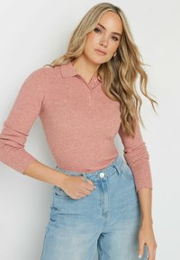 Ribbad, rosa långärmad polotröja med krage och placket med fyra knappar, i kombination med ljusblå hög midja denimjeans.