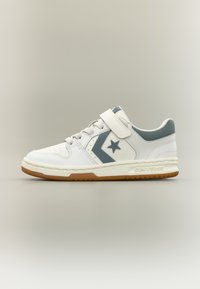 Λευκό χαμηλό αθλητικό παπούτσι με γκρι λογότυπο αστεριού, βέλκρο ρυθμιζόμενο, κορδόνια μπροστά και καουτσούκ σόλα σε ουδέτερο φόντο.