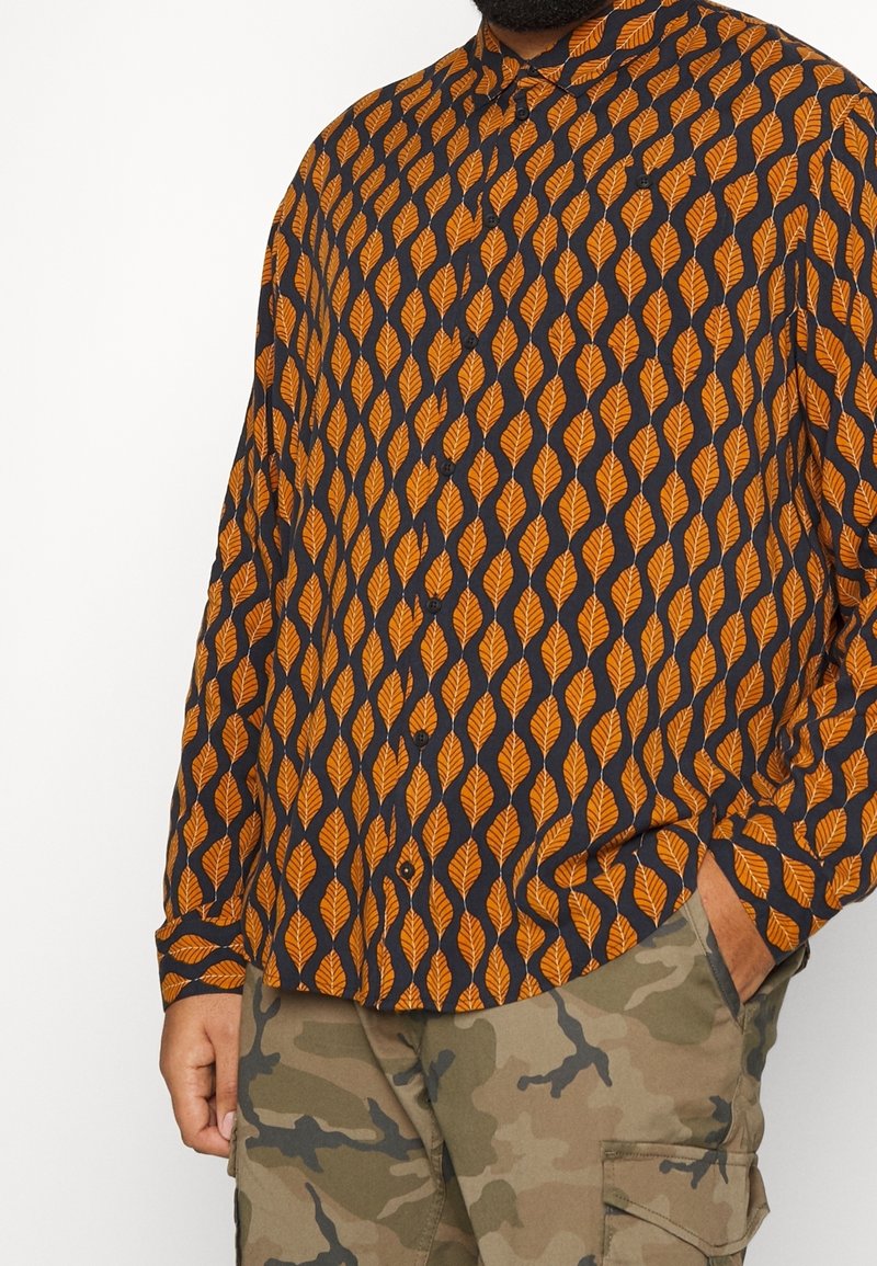 Chemise à manches longues avec un motif de feuilles orange sur un fond bleu marine. Conception boutonnée avec un col et une coupe décontractée.