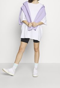 Oversized white T-shirt, black bike shorts, and pastel lilac sweater draped over shoulders. White sneakers with light-colored soles.