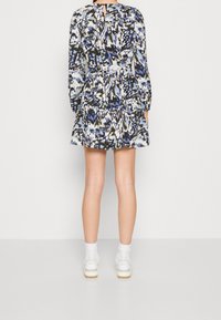 Monivärinen mekko, jossa on pitkät hihat. Mukana kerrostettu helma, takana avainaukko ja abstrakti sininen, musta ja valkoinen kuvio.