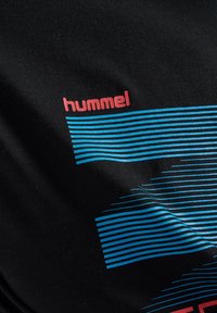 Zwarte t-shirt met het merk "hummel" in het rood, met blauwe horizontale strepen en gestileerde lijnen over het stoffen oppervlak.