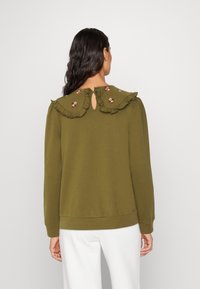 Felpa verde oliva con collo arricciato, ricamo floreale sul collo, chiusura posteriore a occhiello e polsini e orlo a coste.