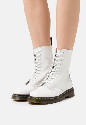 Botas de tornozelo em couro branco com atacadores na frente, bico redondo, costura amarela e sola texturizada preta. Detalhe de design em cima com bordas recortadas.