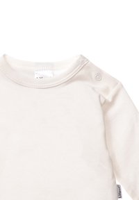 Helle, weiche Baumwollbluse mit langen Ärmeln, rundem Ausschnitt und Druckknöpfen an der Schulter für ein einfaches An- und Ausziehen.