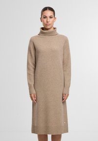 Strickkleid in Beige mit hohem Rippkragen, langen Ärmeln und einem Rippbund. Beinhaltet einen kleinen Akzentknopf am unteren Ende.