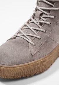 Jasnoszare zamszowe botki do kostki z dopasowanymi płaskimi sznurówkami, teksturowaną gumową podeszwą oraz subtelnymi detalami w szwie po bokach.