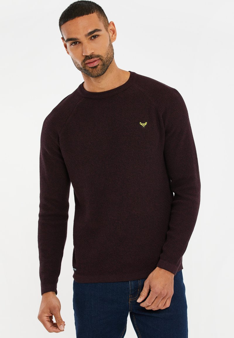 Pullover a maglia color bordeaux con finitura testurizzata, scollatura a girocollo e maniche raglan. Presenta un piccolo logo giallo sul petto.