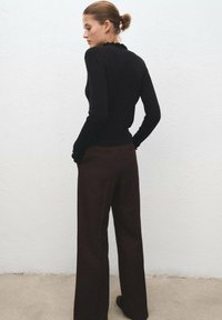 Maglione nero a coste con scollatura a onda, abbinato a pantaloni larghi a vita alta marroni. Texture lisce e silhouette aderente.