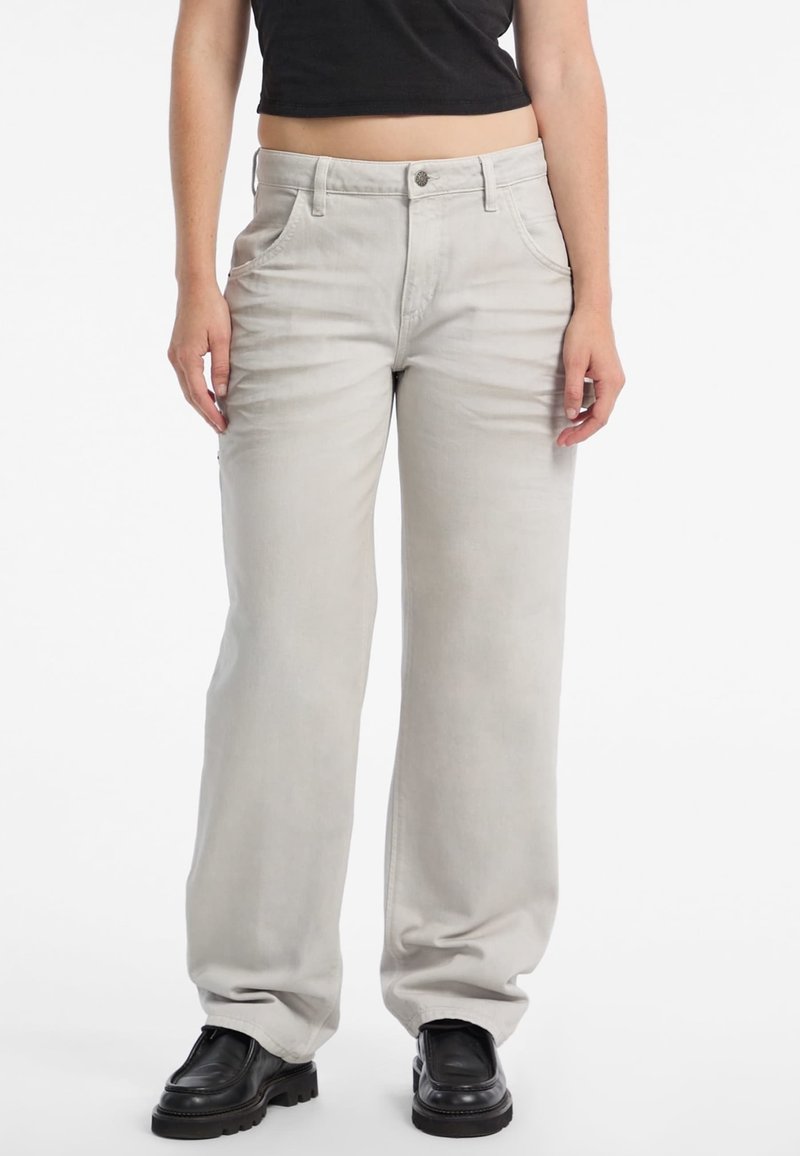 Jeans a gamba larga grigio chiaro in denim, con chiusura anteriore a bottoni, due tasche frontali e una texture leggermente sbiadita. Scarpe nere in vista.