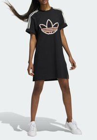 Abito t-shirt corto nero con maniche corte e fessure laterali, caratterizzato da un logo Adidas ricamato multicolore sulla parte anteriore e tre strisce bianche sulle maniche.