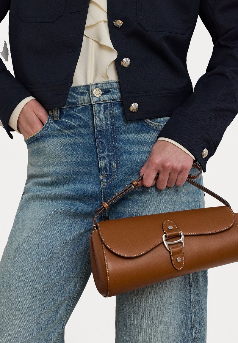 Brun lærveske med klaffelukking, sølvfarget hardware og avtakbar stropp. Kombinert med en mørk jakke og lyse denimjeans.