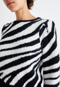 Maglione a strisce bianche e nere caratterizzato da una morbida e soffice trama, con scollatura rotonda e audaci motivi di strisce irregolari.