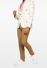 Biała marynarka z kolorowymi tropikalnymi i owocowymi wzorami, brązowe spodnie i białe tenisówki. Guziki na marynarce dodają detali i kontrastu.