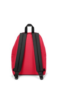 Mochila de tela roja con asas acolchadas negras, un asa superior y una forma redondeada con líneas limpias y sin herrajes visibles.
