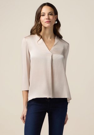 Silky, light pink blouse with a V-neck, 3/4 sleeves, and a loose fit, paired with dark blue jeans. Smooth texture and draped design.