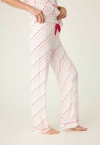 Bílé pyžamové kalhoty s růžovými a červenými vzory srdcí, elastický pás se zavazováním na růžovou stuhu, rovný střih a červený lem na spodním okraji.