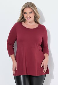 Bordeauxfarbener Langarm-Oberteil mit Rundhalsausschnitt, leicht ausgeflocktem Saum und weicher Textur, kombiniert mit schwarzen Skinny-Jeans.