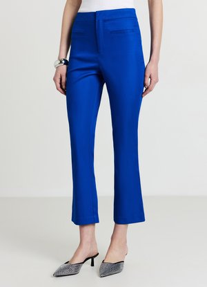 Pantaloni sartoriali blu elettrico con una texture liscia, tasche laterali e orlo svasato corto. Abbinati a mule nere e bianche decorate.