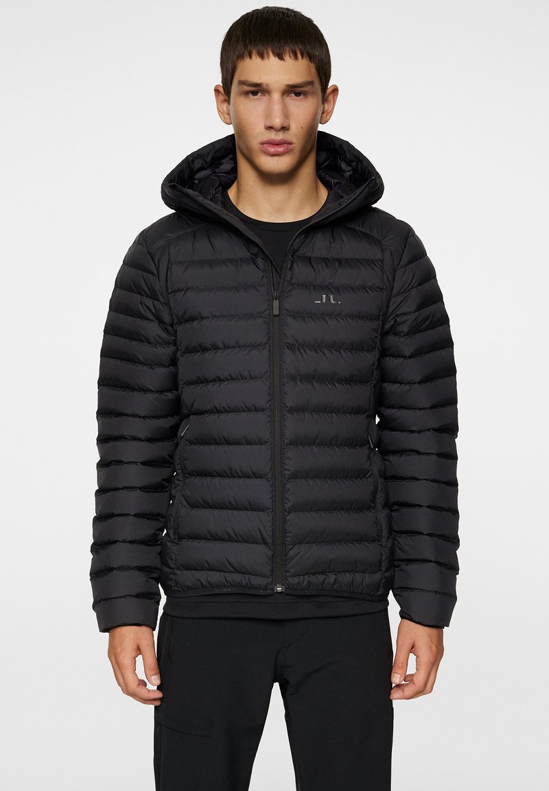 Svart vadderad jacka med dragkedja framtill och huva. Har en kviltad design och en diskret logotyp på bröstet. Texturerat, lättviktigt material.