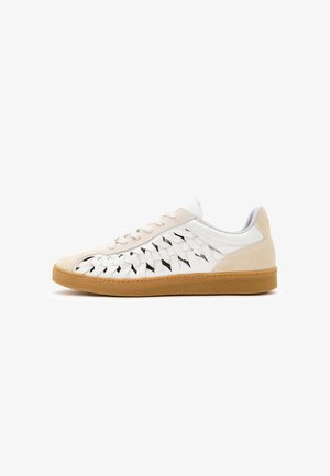 Zapatilla deportiva de cuero blanco con paneles laterales tejidos, acentos en ante beige en el talón y la punta, cordones blancos y suela de goma color caramelo, mostrada de perfil.