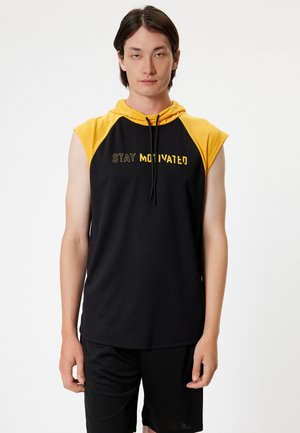 Sudadera sin mangas negra con acentos amarillos y cordón. Presenta el texto "MANTENTE MOTIVADO" en el frente. Tela suave, corte atlético.