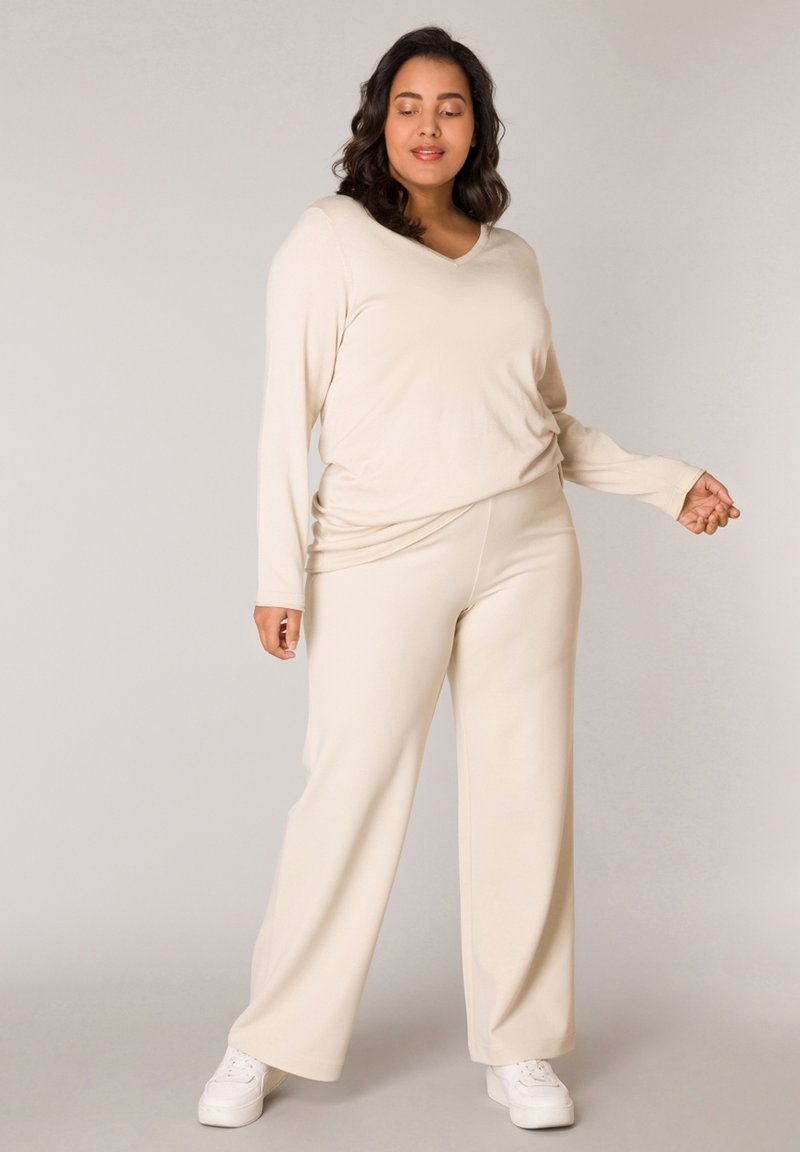 Beige long-sleeve V-neck top with loose fit, paired with wide-leg trousers in matching color, complemented by white sneakers. Smooth texture.