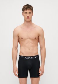 Boxers pretos da Nike com um cós de logótipo em contraste. O material parece liso e elástico, oferecendo um design ajustado.