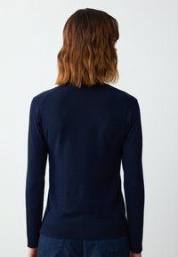 Granatowy sweter z dzianiny z długimi rękawami i okrągłym dekoltem, o gładkiej fakturze i ściągaczu w talii oraz przy mankietach.