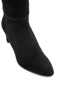 Czarny zamszowy botek za kostkę z szpiczastym noskiem i niskim obcasem. Charakteryzuje się bezszwową konstrukcją i widocznym przeszyciem wzdłuż cholewki.