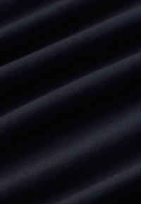 Dunkelblaues Baumwollgewebe mit einer weichen Textur, das dezente Rippmuster und glatte, sanft geschwungene Falten auf der Oberfläche aufweist.