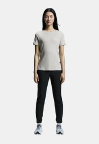 Camiseta gris claro de manga corta con cuello redondo; combinada con pantalones negros ajustados y zapatillas deportivas blancas con acentos negros.