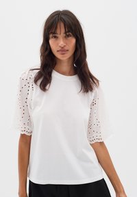 T-shirt bianco con maniche corte ricamate e trasparenti, con motivi ritagliati. Tessuto di cotone morbido con vestibilità rilassata e scollatura rotonda.