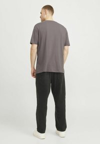 Grå bomulds t-shirt med rund hals, parret med løse sorte fløjl bukser. Modellen står med ryggen til og viser minimal detaljering.