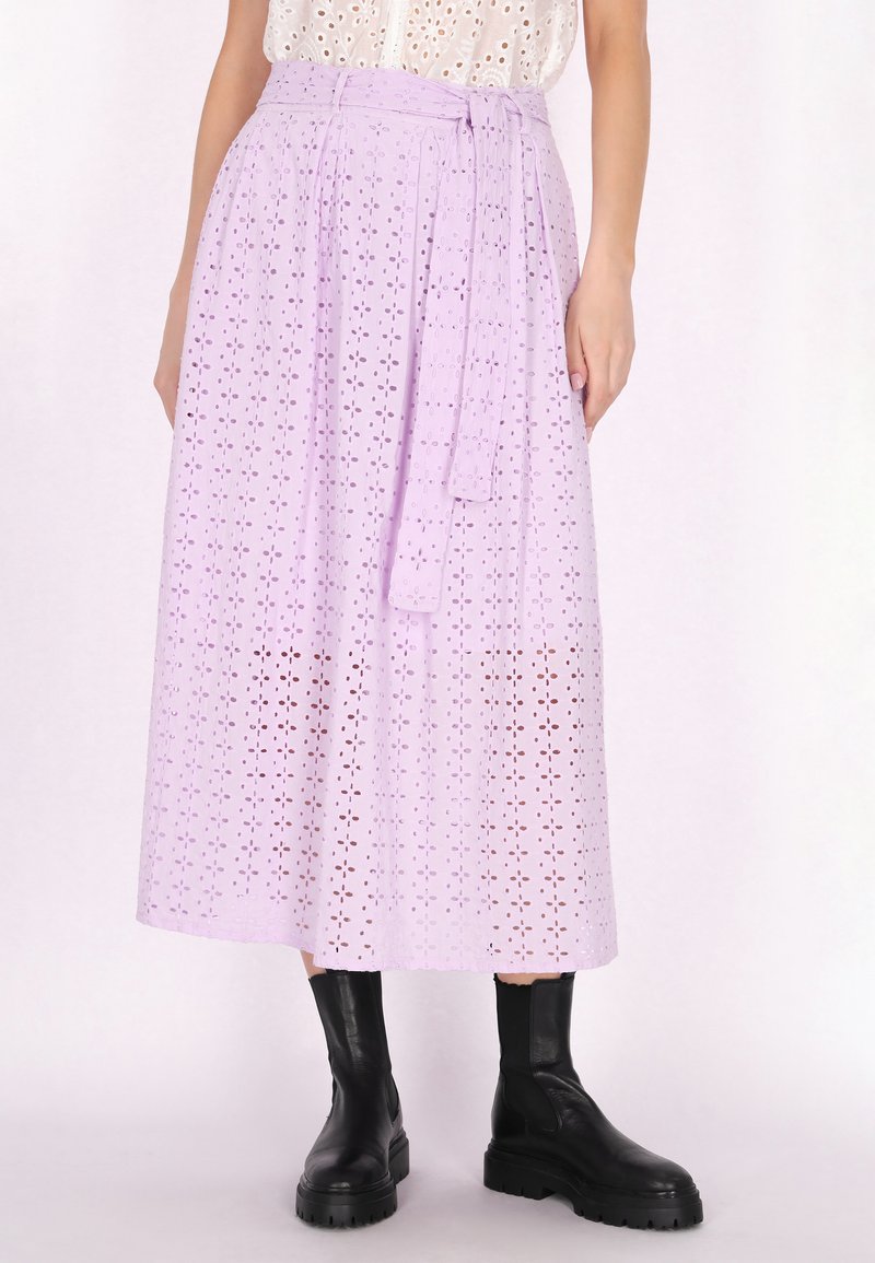 Gonna midi color lilla in pizzo con vita a laccio, caratterizzata da un motivo floreale perforato e una silhouette fluente. Abbinata a stivali neri alla caviglia.